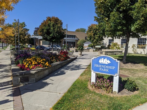 friendship park sign with flowers in raised beds sidewalk trees and library